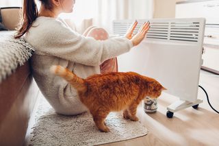 Frau sitzt mit Katze vor Heizung