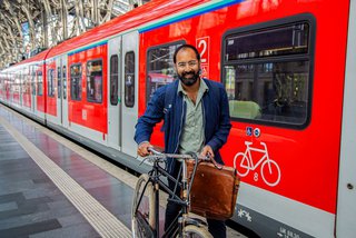 Mann schiebt Fahrrad neben Zug am Bahnsteig 
