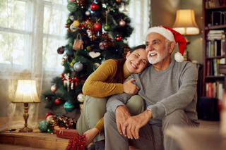 Enkelin und Opa sitzen beieinander vorm Weihnachtsbaum und freuen sich Enkelin und Opa sitzen beieinander vorm Weihnachtsbaum und freuen sich