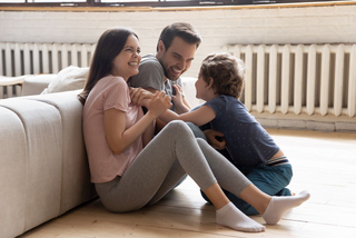 Mutter, Vater und Kind sitzen im Wohnzimmer vor einem Heizkörper