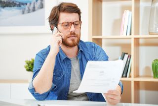 Besorgter Mann am Telefon mit Rechnung in der Hand