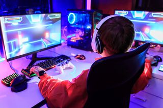 Junge mit Kopfhörern an Gaming-PC mit zwei Bildschirmen