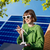 Frau sitzt auf Dachterrasse vor Solarpanels mit Windradmodel auf Tisch.