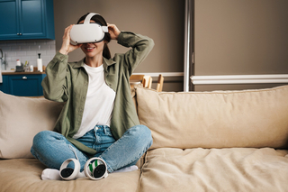 Junge Frau sitzt mit VR-Brille auf einem Sofa