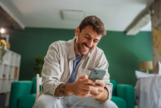 Mann schaut lachend auf Handy Mann schaut lachend auf Handy