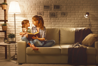 Mutter und Tochter lesen auf der Couch bei gemütlicher Beleuchtung