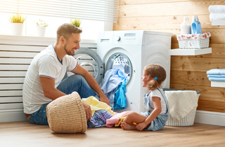 Vater und Tochter sitzen vor der Waschmaschine mit Wäsche