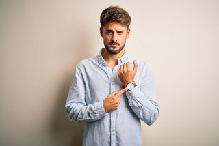 Mann zeigt verärgert auf seine Armbanduhr