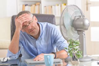 Mann sitzt schwitzend vorm Ventilator