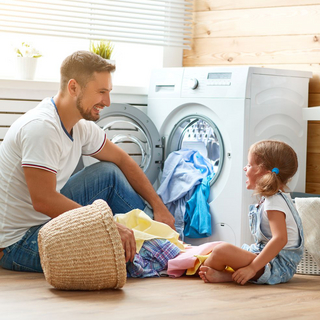 Vater und Kind sitzen vor der Waschmaschine und befüllen sie mit Wäsche